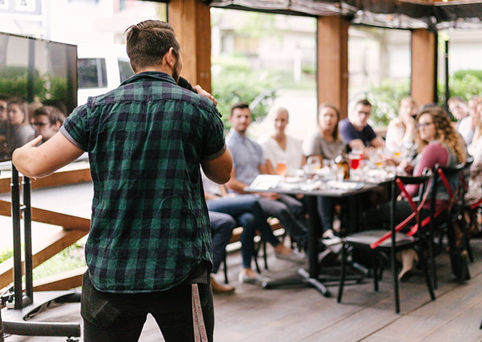 A presenter speaking to a number of people sitting at a table